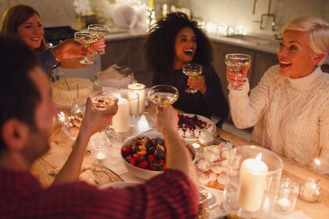 Nadšení priatelia opekajú poháriky šampanského pri vianočnej večeri pri sviečkach