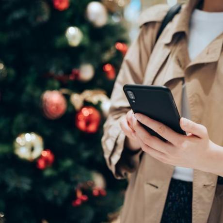 orezaný záber a stredná časť ženy používajúcej smartfón pred farebným vianočným stromčekom počas sviatočného vianočného obdobia