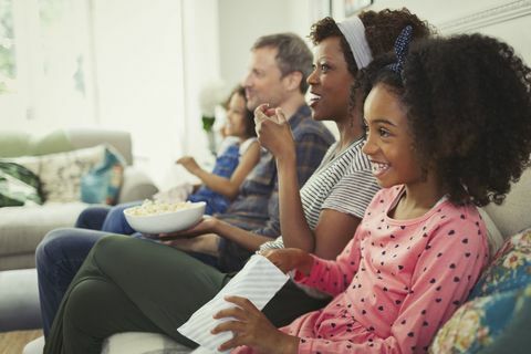 Mladá multietnická rodina pozerá film a jesť popcorn na pohovke