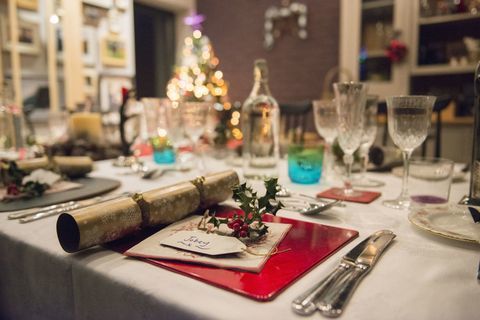 Stôl položený na vianočné jedlo so striebornými a krištáľovými poháre a vianočný stromček v pozadí.