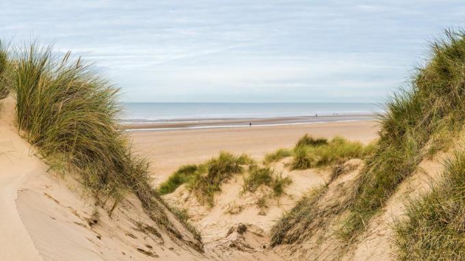 panoráma s viacerými obrázkami zachytená medzi dvoma vrcholmi na piesočných dunách hľadiacich dolu na ľudí kráčajúcich po pláži Formby neďaleko Liverpoolu