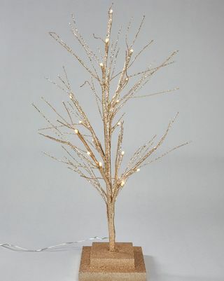 Malá šampanská zlatá batéria fungovala s predsvieteným vetvičkovým vianočným stromčekom