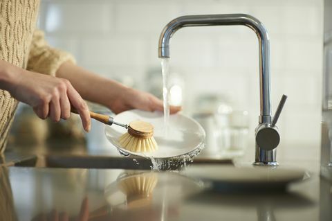 žena používa bezplastovú kefu na čistenie riadu v kuchynskom dreze zblízka