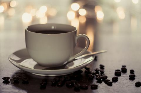 Šálka ​​a podšálka obsahujúca kávu sa posadila na stôl rozptýlený z kávových zŕn.