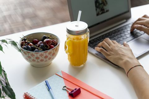 Detailný záber na ženu pomocou notebooku pri stole s pomarančovým džúsom a ovocím