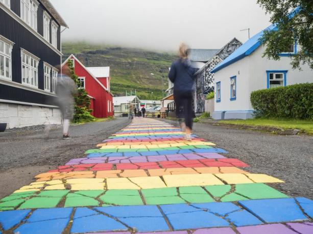 Island, Seydisfjordur, ľudia kráčajúci po dúhovej asfaltovej ceste uprostred odľahlého mesta