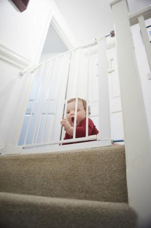 Detská bezpečnostná brána na schodoch: Chlapček na odpočívadle svojho domu. Je za detskou bezpečnostnou bránou, ktorá ho bráni pred nebezpečenstvom zo schodiska.