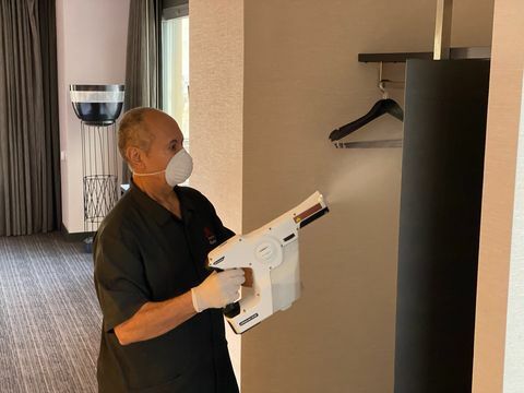 muž v hotelovej izbe pomocou rozprašovača na dezinfekciu otvorenej skrine