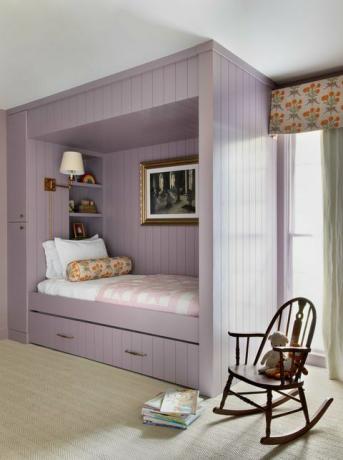 detská izba, fialová posteľ, hnedé hojdacie kreslo, úložný priestor pod posteľou, kvetinové závesy